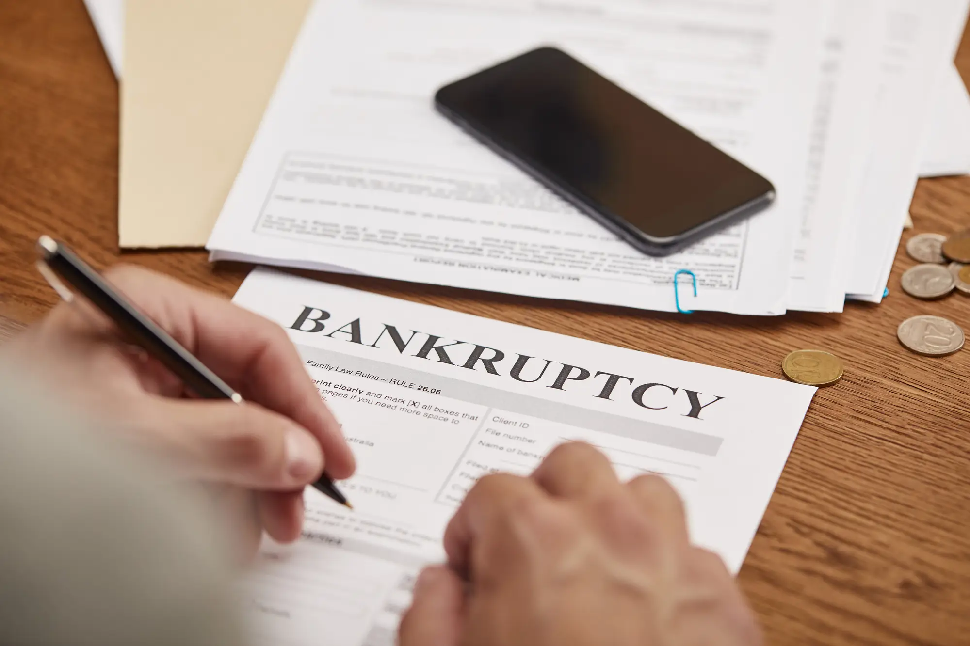 partial-view businessman filling bankruptcy form with smartphone on wooden table